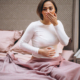 Young woman sitting up in bed with stomach issues