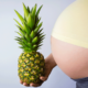 Closeup of a woman holding a pineapple in front of her pregnant belly.