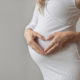 Pregnant woman making heart sign over her belly.